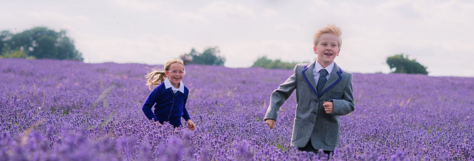 Children dressed in uniform, running through a field of purple flowers