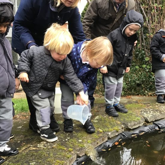 Children looking into the pond with the teachers on hand