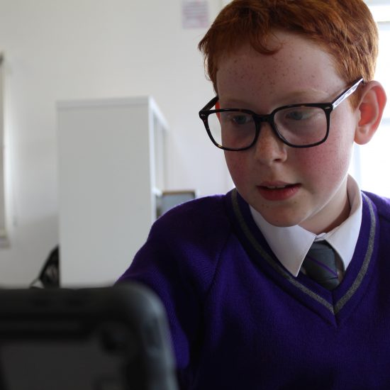A young child wearing glasses and in his purple uniform using a tablet in lessons