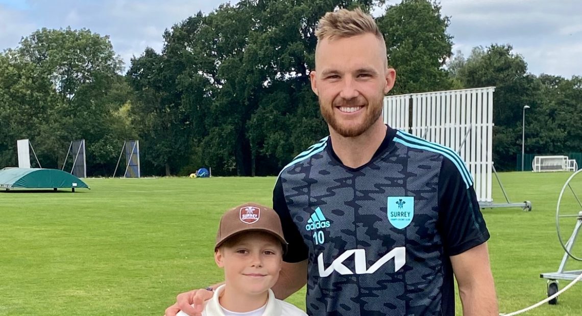 A young boy smiles next to a cricketer
